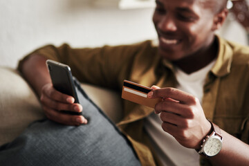 When youve just stumbled upon the biggest sale ever.... Cropped shot of a handsome young man smiling while using a smartphone and a credit card to shop online in his living room at home.