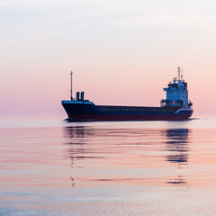 Wall Mural - Large cargo ship sailing in the Baltic sea at sunset. Soft golden sunlight. Concept seascape. Panoramic view from the sailing boat. Freight transportation, nautical vessel, logistics