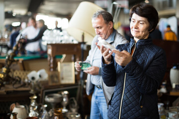 Wall Mural - smiling elderly woman choosing interesting souvenirs at traditional flea market