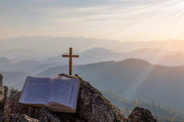 Wall Mural - crucifix symbol and bible on top mountain with bright sunbeam on the colorful sky background