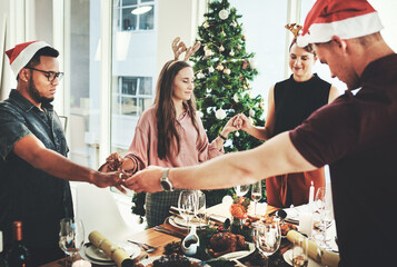 Wall Mural - Their tradition is to say grace before digging in. Cropped shot of a group of young friends saying grace while dining together at Christmas.