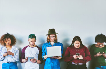 Poster - Consumed with media. Studio shot of a group of young people standing against a wall and using wireless technology.