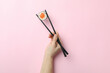 Female hand hold chopsticks with maki on pink background