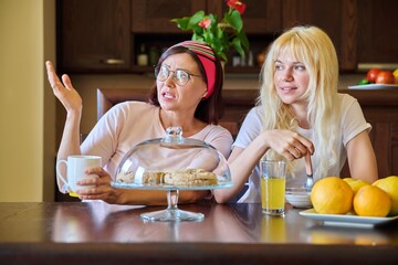 Poster - Mom and teenage daughter eating together, sitting at table at home in kitchen