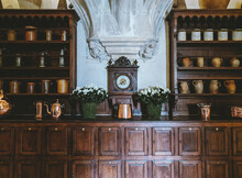 Vintage Clock In A Luxurious Home With Copper Teapots On The Wooden Cupboard And An Arched Ceiling