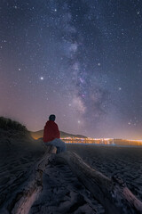 Wall Mural - vertical shot of a person sitting on a wooden branch and looking at a starry sky.