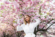 © Denys - A blonde woman in a white shirt poses near the cherry blossoms. Spring mood