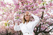 © Denys - A blonde woman in a white shirt poses near the cherry blossoms. Spring mood