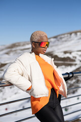 Sticker - Vertical shot of an African American woman leaning on a fence in the background of mountains.