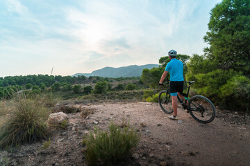 Fit male in a blue shirt riding a bike on a dirt trail