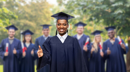 Wall Mural - education, graduation and people concept - happy graduate student woman in mortarboard and bachelor gown giving her hand for handshake over group of bachelors at park on background