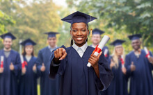 Education, Graduation And People Concept - Happy Graduate Student Woman In Mortarboard And Bachelor Gown With Diploma Pointing Finger To Camera Over Group Of Bachelors At Park On Background