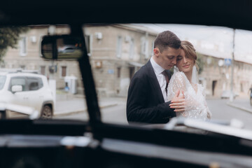 Wall Mural - Wedding of a beautiful, stylish couple, a bride in a white wedding dress and a groom in a black suit, tuxedo, in a black retro car.