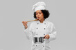 culinary and people concept - female chef in toque with saucepan and spoon cooking and tasting food over grey background