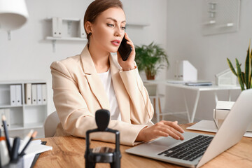 Wall Mural - Female notary public talking by phone while working on laptop in office