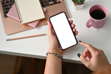 Poster - Top view of hand holding a white blank screen smartphone, pencil and a cup of coffee with note books and flower on the side, for business and technology concept.