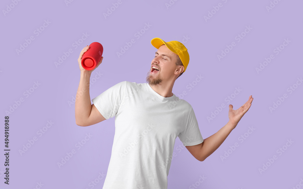 Man holding wireless portable speaker and singing on violet background