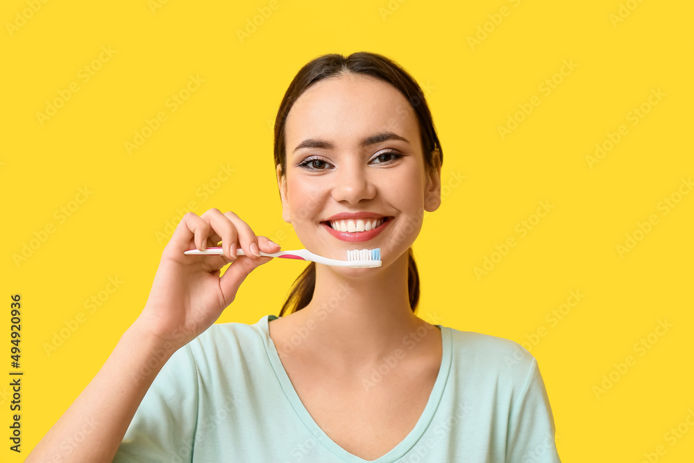 Smiling young woman with tooth brush on yellow background