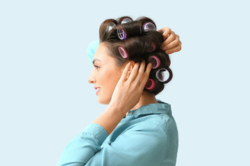 Wall Mural - Beautiful young woman in hair rollers on light background