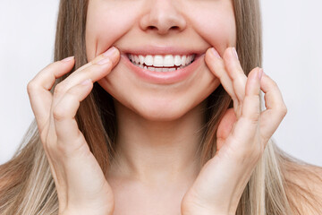 Wall Mural - Young caucasian blonde woman demonstrating the beautiful smile with her hands isolated on a white background. Teeth whitening. Oral hygiene, dental health care, perfect even teeth. Dentistry