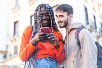 Happy multi ethnic young couple looking mobile phone – interracial people using smartphone – multicultural boyfriend and girlfriend watching cellphone in hand – mixed race people send sms with cell ph