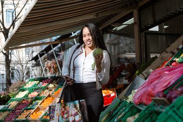 Lifestyle portrait of Hispanic woman walking with bag on street with fruit bowls in city of Lyon