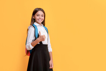 Wall Mural - happy teen girl in school uniform carry backpack showing thumb up, copy space, september 1