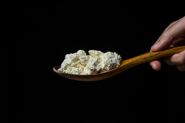 Wall Mural - Curd on a black background. Healthy and tasty dairy product. Man's hand holding a spoon of cottage cheese