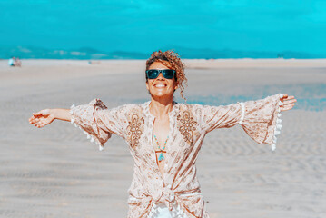 Happy standing pretty adult woman at the beach outstretching arms with tropical summer holiday beach and ocean in background. Concept o travel and wanderlust active female solo people lifestyle