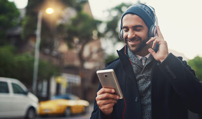 Poster - Music on....World off. Cropped shot of a fashionable young man listening to music on his phone while out in the city.