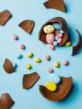 Easter Chocolate Egg Broken In Pieces With Small Multicolor Eggs Inside On Pastel Blue Background. Creative Easter Holiday Or Sweeties Concept. Minimal Festive Greeting Card.