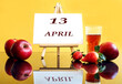© MARYIA - Calendar for April 13: an easel with the inscription 13, april, apples and strawberries next to it, a glass of freshly squeezed juice, yellow background, side view