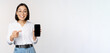 Enthusiastic young asian woman pointing finger at smartphone screen, showing advertisement on mobile phone, white background
