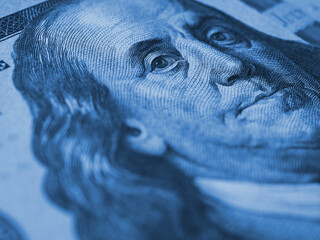 Wall Mural - American paper money background. A $100 bill with focus on Benjamin Franklin eye. US banknote close up. Dark blue tinted wallpaper about economy and the USA dollar. Macro