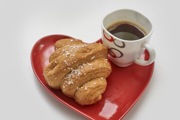 Wall Mural - Fresh and appetizing croissant with a cup of coffee on a red heart-shaped plate