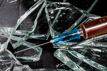 Medical Syringe With Drug Close-up On Broken Glass. Drug Addiction Concept