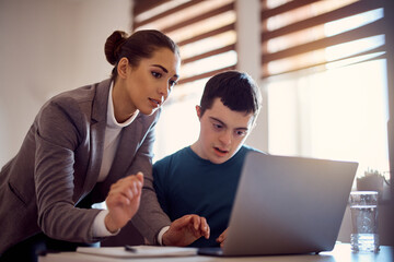 Young man with down syndrome learning to use laptop with help of his tutor at home.