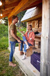 Young attractive tourist cheerful couple having a conversation in front of wooden cottage. Woman explaining something, hand gesture. Beuatiful moments. Vacation, holiday, togetherness concept.