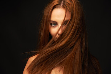  Showing off her shiny locks. Portrait of a beautiful redhead with her hair covering her face on a black background.