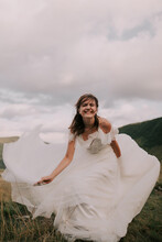 Happy Bride In White Wedding Dress Smiling Against The Backdrop Of Mountains.