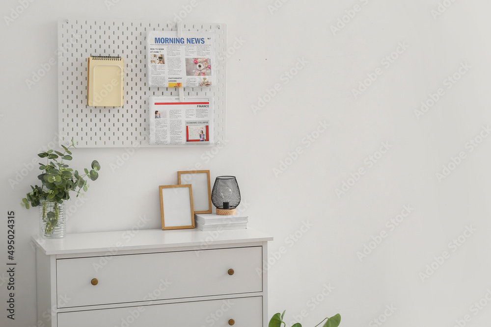 Chest of drawers with frames and pegboard hanging on light wall
