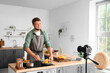 © Pixel-Shot - Young man cooking corn and recording video tutorial in kitchen