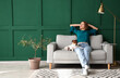 © Pixel-Shot - Young woman with Jack Russel terrier resting on grey sofa near green wall