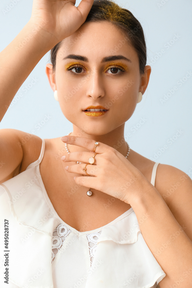 Attractive young woman with unusual shiny makeup on light background