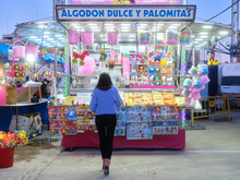 Young Woman Walking Towards A Cotton Candy And Popcorn Stand At An Evening Fair