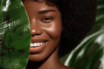 Wall Mural - african american young woman smilling, close up potrait against green tropacal leaf. natural skin ca