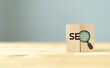 © Parradee - SEO, Search Engine Optimization ranking concept.  Digital marketing strategy of promote traffic to website. Wooden cubes with magnifying glass icon and alphabets abbreviation SEO on grey background.