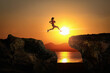 © jayzynism - Silhouette of runner jumping over gap between cliff with evening sunset sky on background.