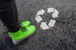 legs in shoes is standing next to recycle sign on road asphalt 