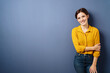 © contrastwerkstatt - young relaxed business woman with yellow blouse stands in front of blue background